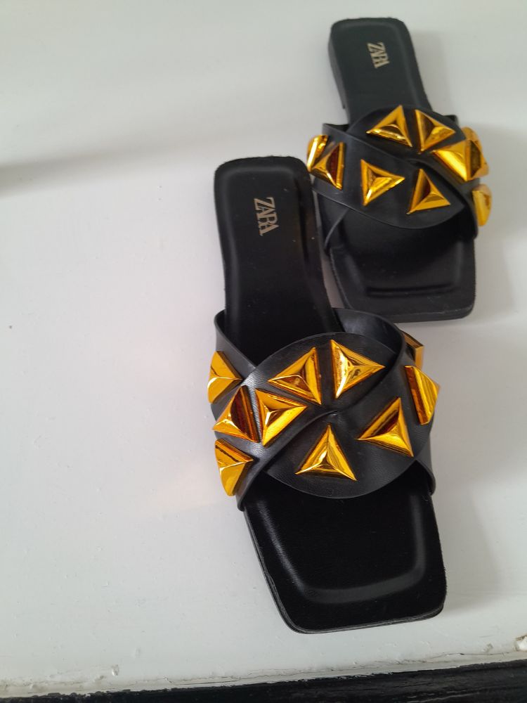 Flat black leather sandals with a braided design and gold studs along the top.